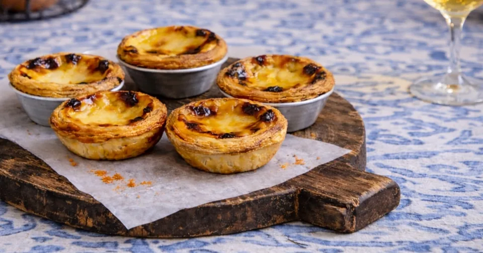 Custard tarts on a wooden board on a blue tiled table