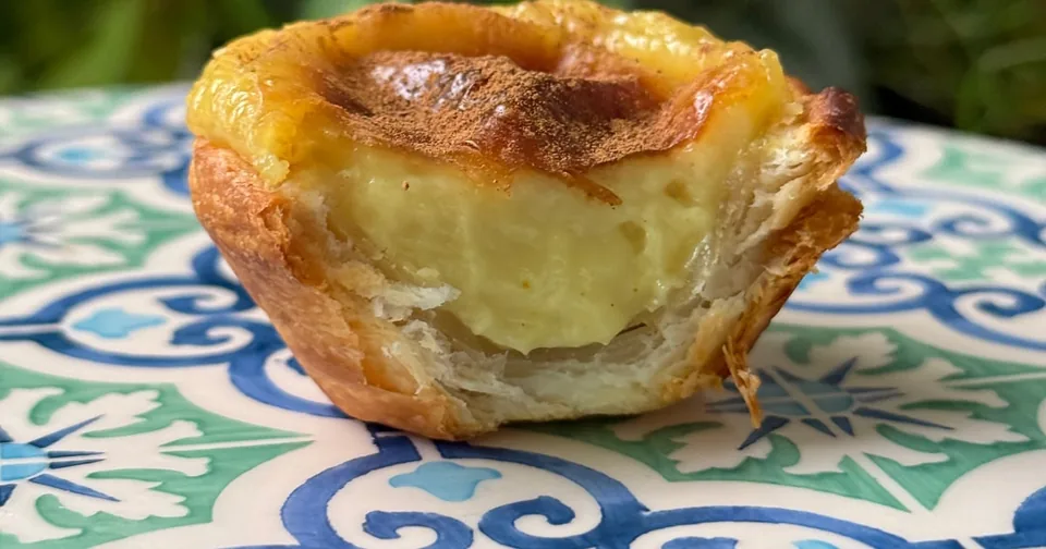 A single custard tart with blistered top on a blue and white tiled plate