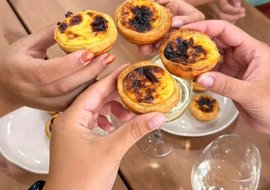 Hands holding warm custard tarts over a table